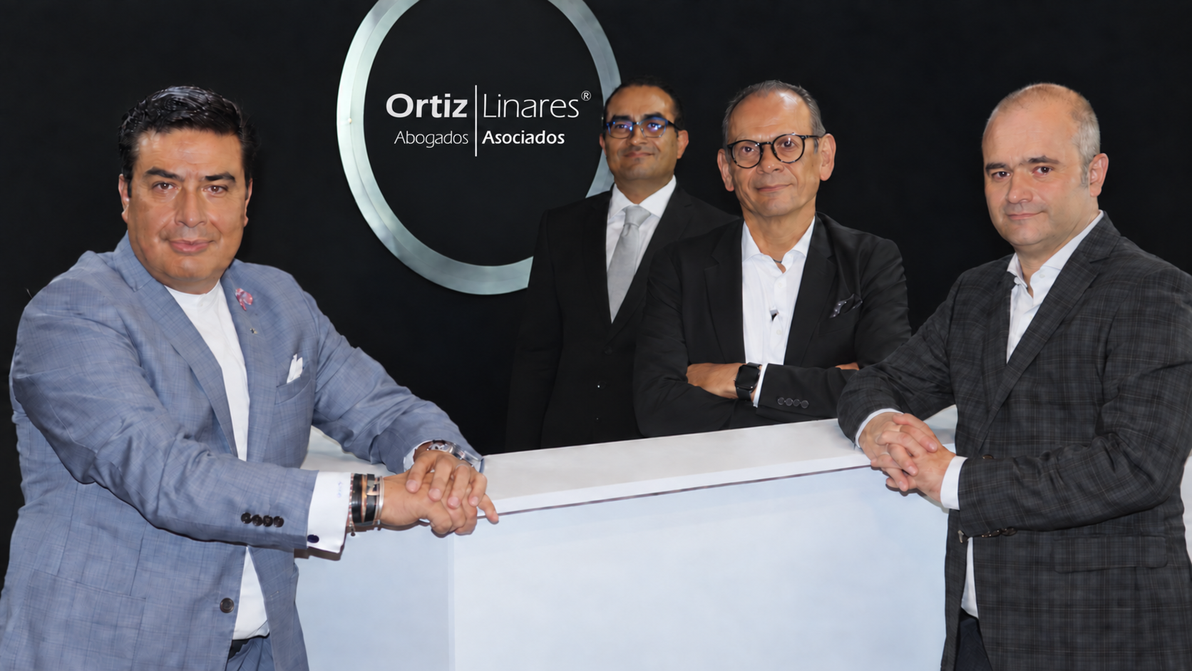 Socios de Ortiz Linares frente al logotipo institucional